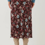 A person shown from the back wearing a dark floral midi skirt with a blue sweater and beige heeled boots against a plain light background.