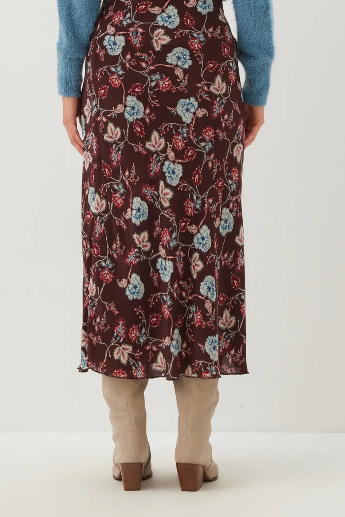 A person shown from the back wearing a dark floral midi skirt with a blue sweater and beige heeled boots against a plain light background.