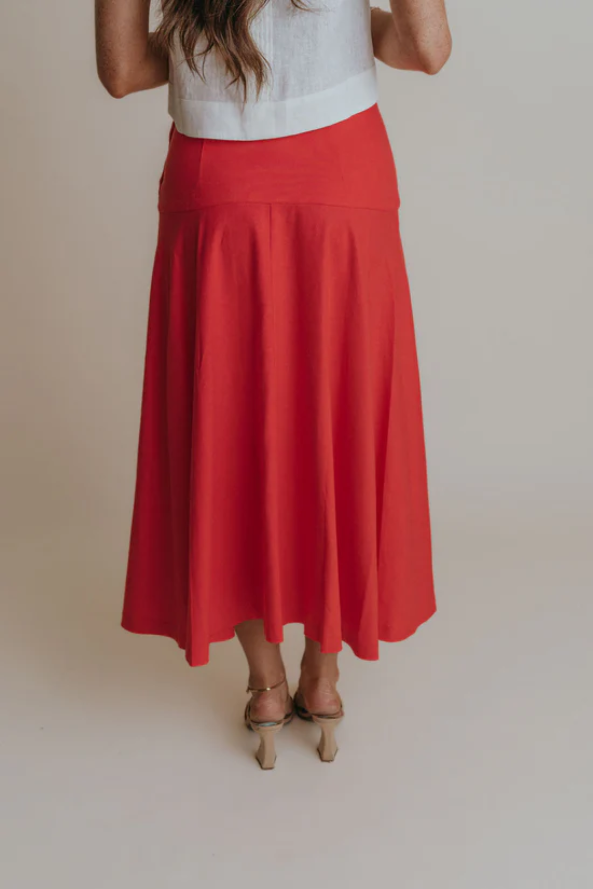back of woman in red skirt on tan background 