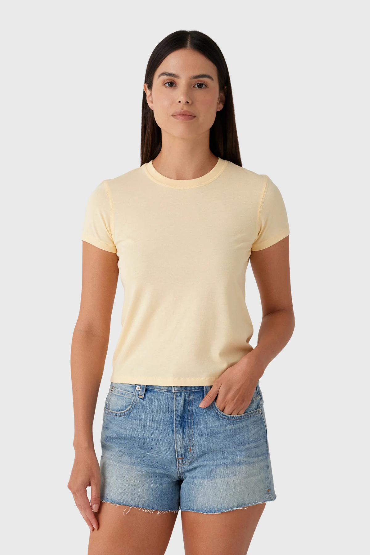 Woman wearing a light yellow t-shirt and denim shorts on a white background
