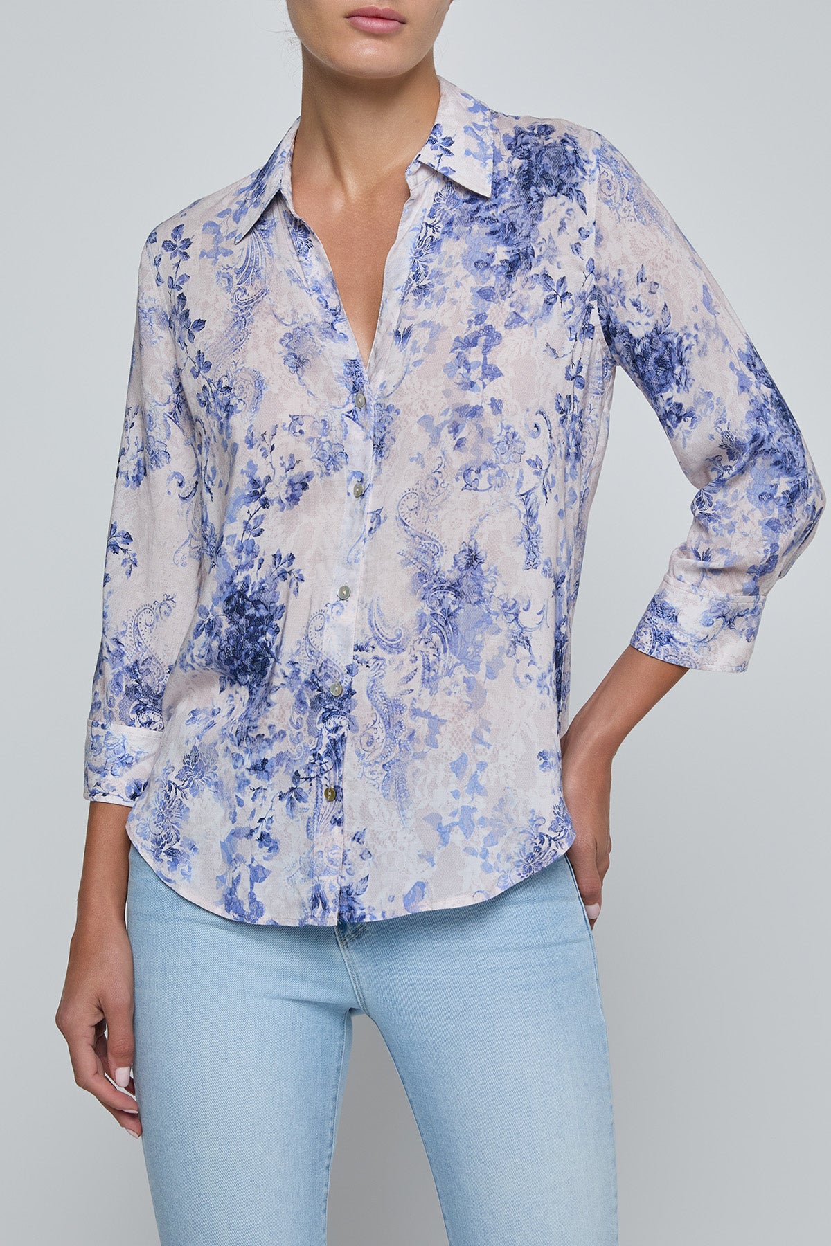 Person wearing a blue floral shirt and light blue jeans on a gray background