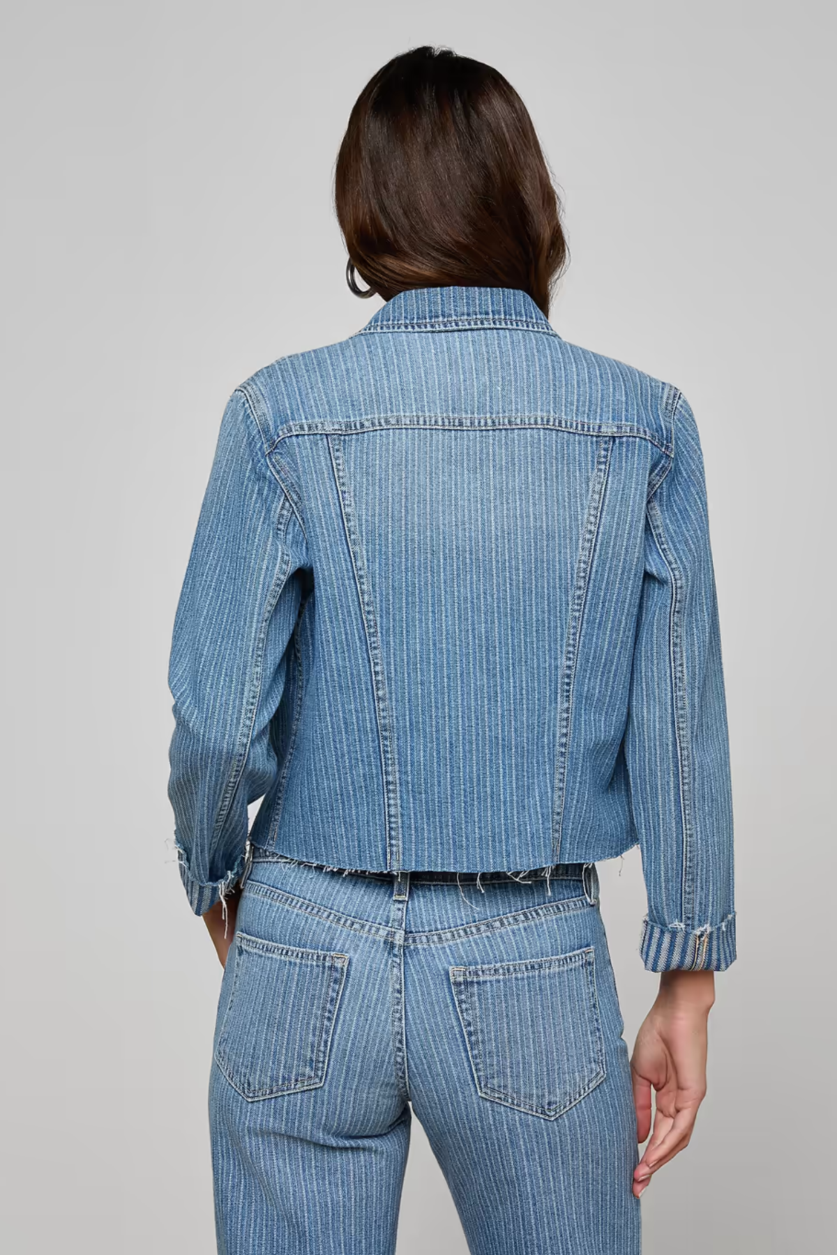 Person wearing a blue denim jacket and pants on a gray background