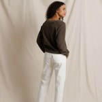 Person wearing a dark sweater and white pants against a beige backdrop