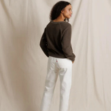 Person wearing a dark sweater and white pants against a beige backdrop
