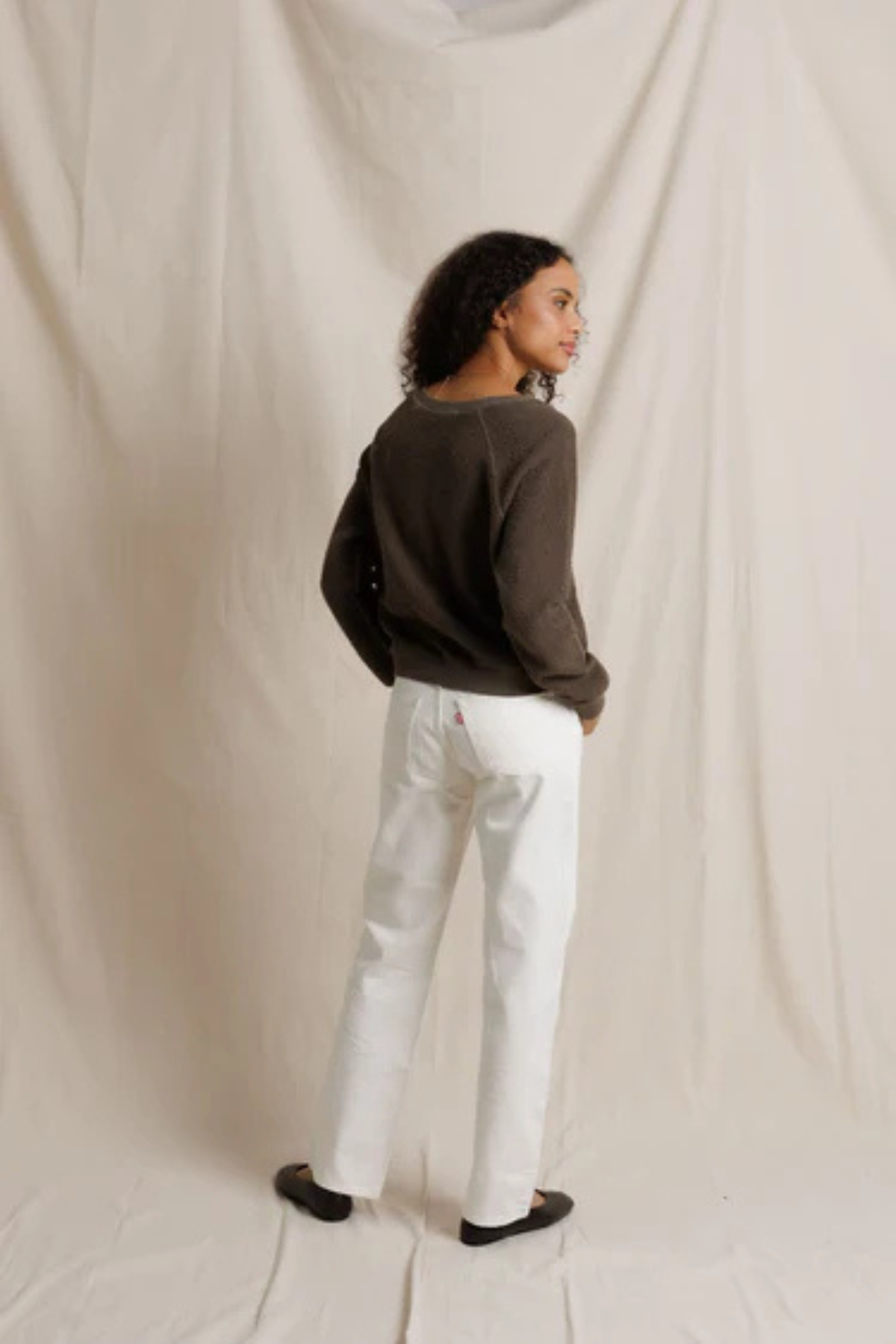 Person wearing a dark sweater and white pants against a beige backdrop