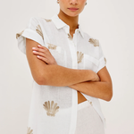 Woman wearing a white shirt with shell patterns on a plain background