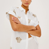 Woman wearing a white shirt with shell patterns on a plain background