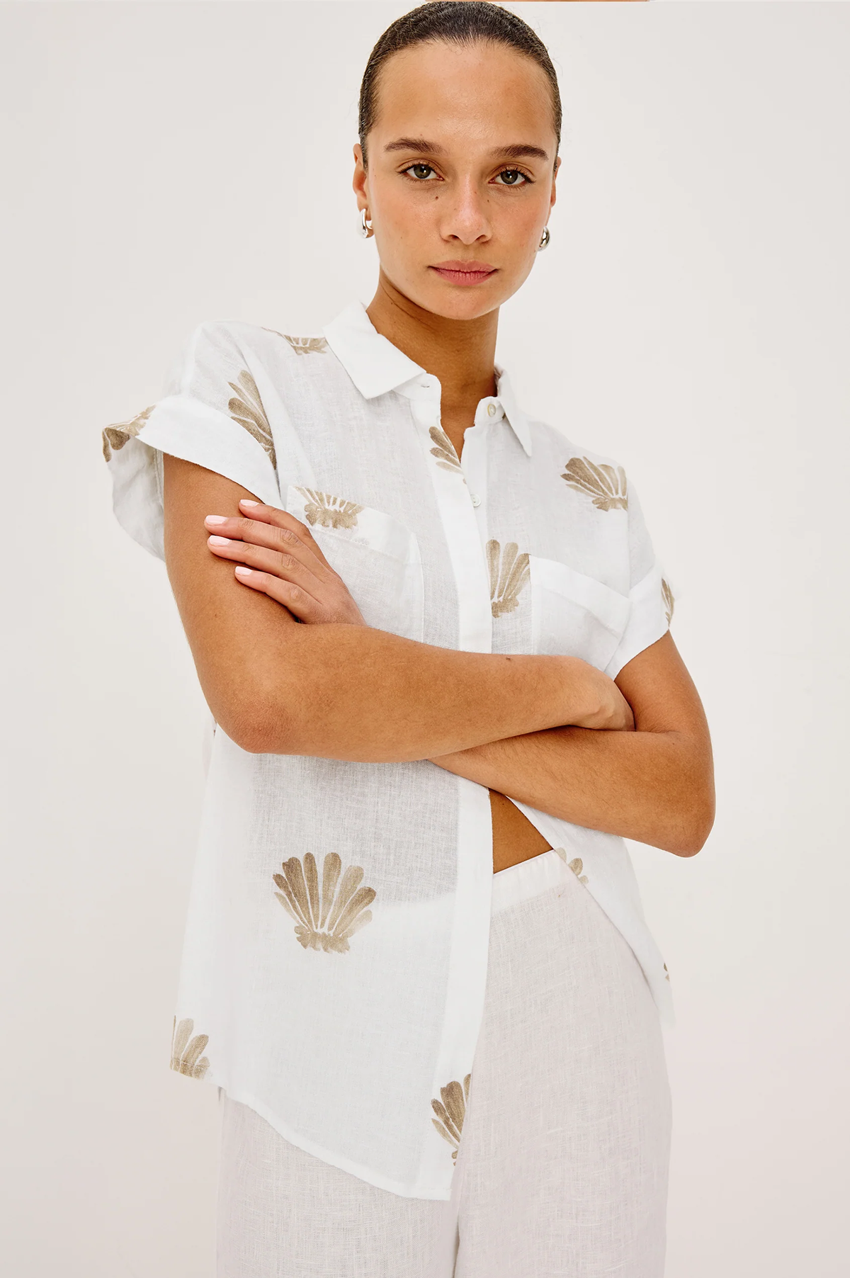 Woman wearing a white shirt with shell patterns on a plain background