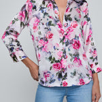 Woman wearing a floral blouse with pink roses and blue jeans on a gray background