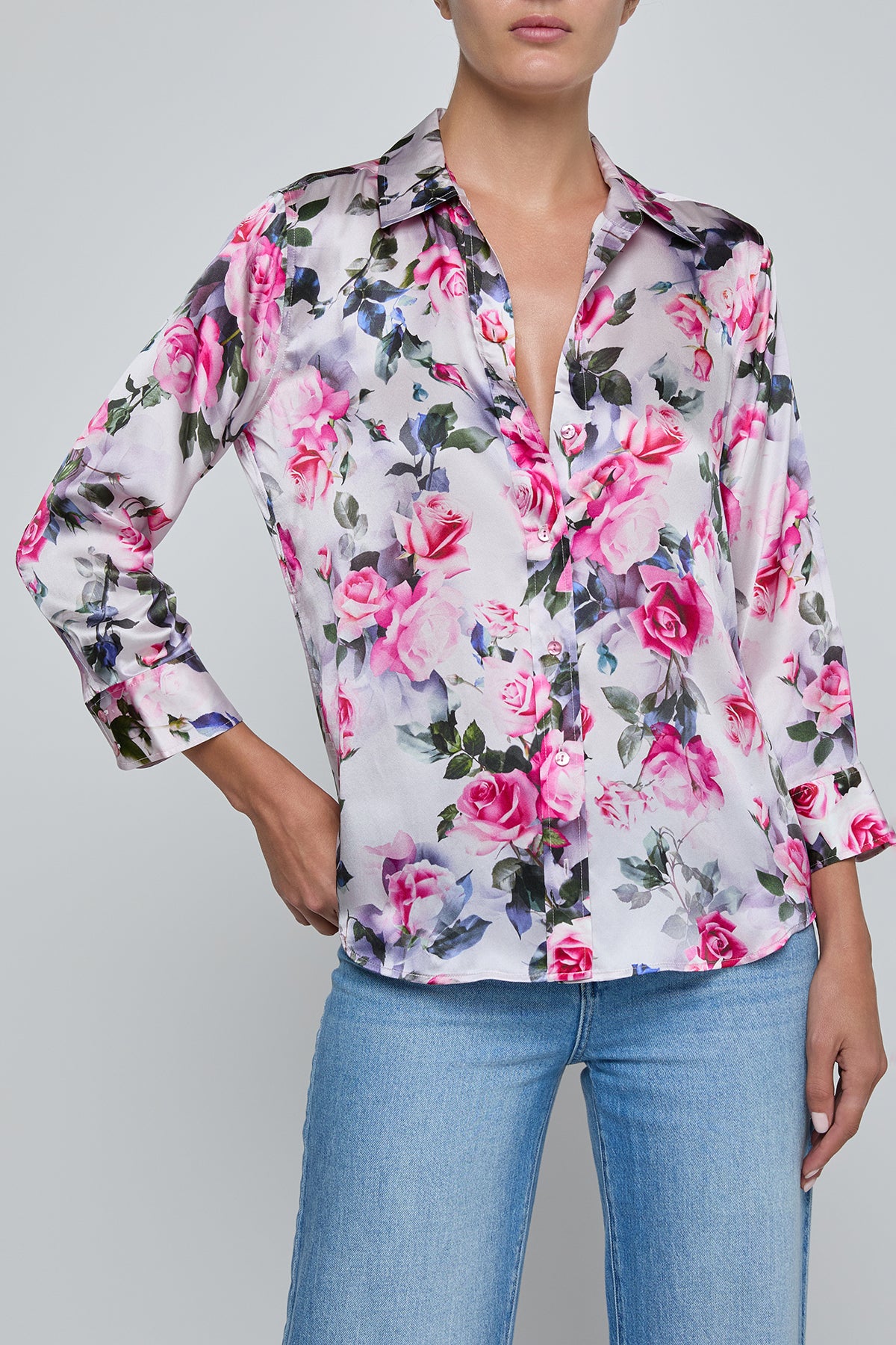 Woman wearing a floral blouse with pink roses and blue jeans on a gray background