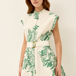 Woman wearing a white dress with green leaf pattern on a plain background