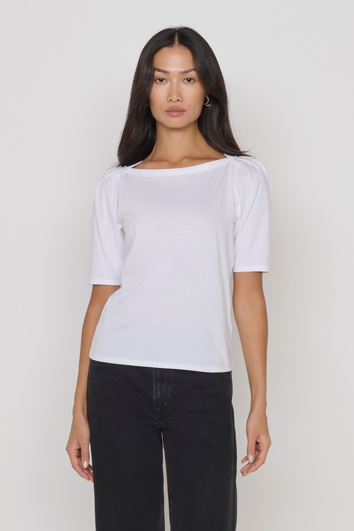 Woman wearing a white t-shirt and black pants against a plain background