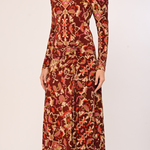 A woman wearing a long-sleeve midi dress with a dense abstract floral and paisley pattern in rust red, orange, brown, and beige, photographed against a plain light background.