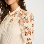 Woman wearing a beige lace blouse against a white background