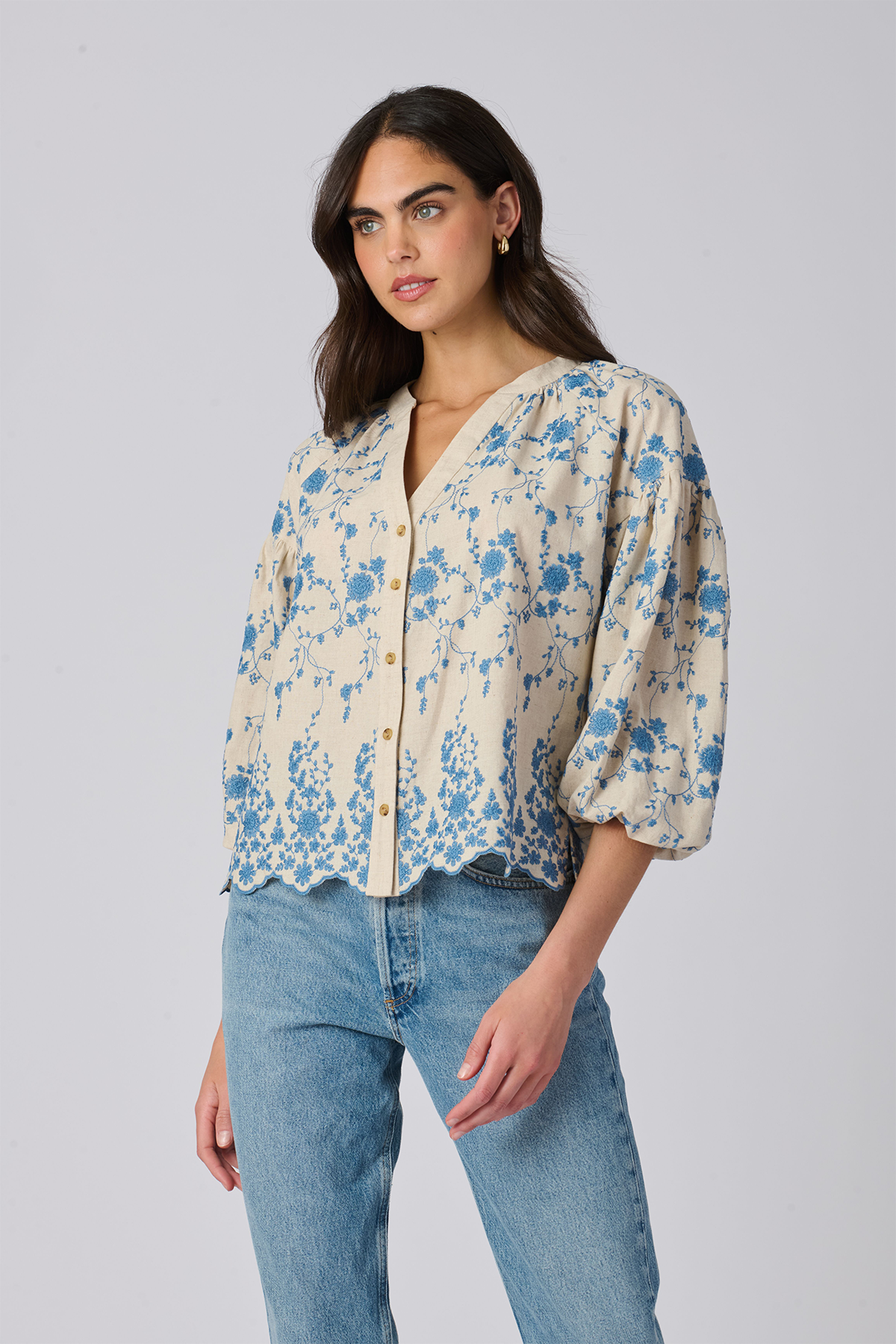 Woman wearing a floral blouse and jeans on a plain background