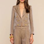A woman modeling a taupe double-breasted blazer and matching wide-leg trousers with prominent gold buttons, set against a solid beige background.