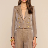 A woman modeling a taupe double-breasted blazer and matching wide-leg trousers with prominent gold buttons, set against a solid beige background.