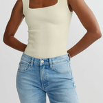 Person wearing a beige tank top and blue jeans on a plain background