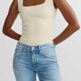 Person wearing a beige tank top and blue jeans on a plain background