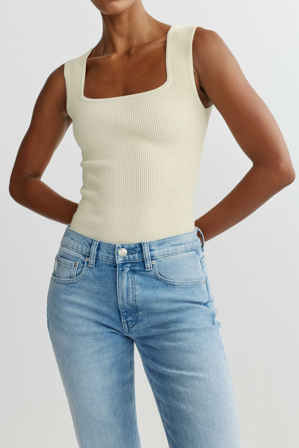 Person wearing a beige tank top and blue jeans on a plain background
