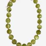 A beaded necklace made of faceted olive green glass beads separated by small gold spacers, with a gold chain extender and clasp, shown on a light gray background.