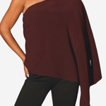 A woman wearing a dark burgundy one-shoulder knit poncho top with black leggings, shown from the neck down against a light gray background.