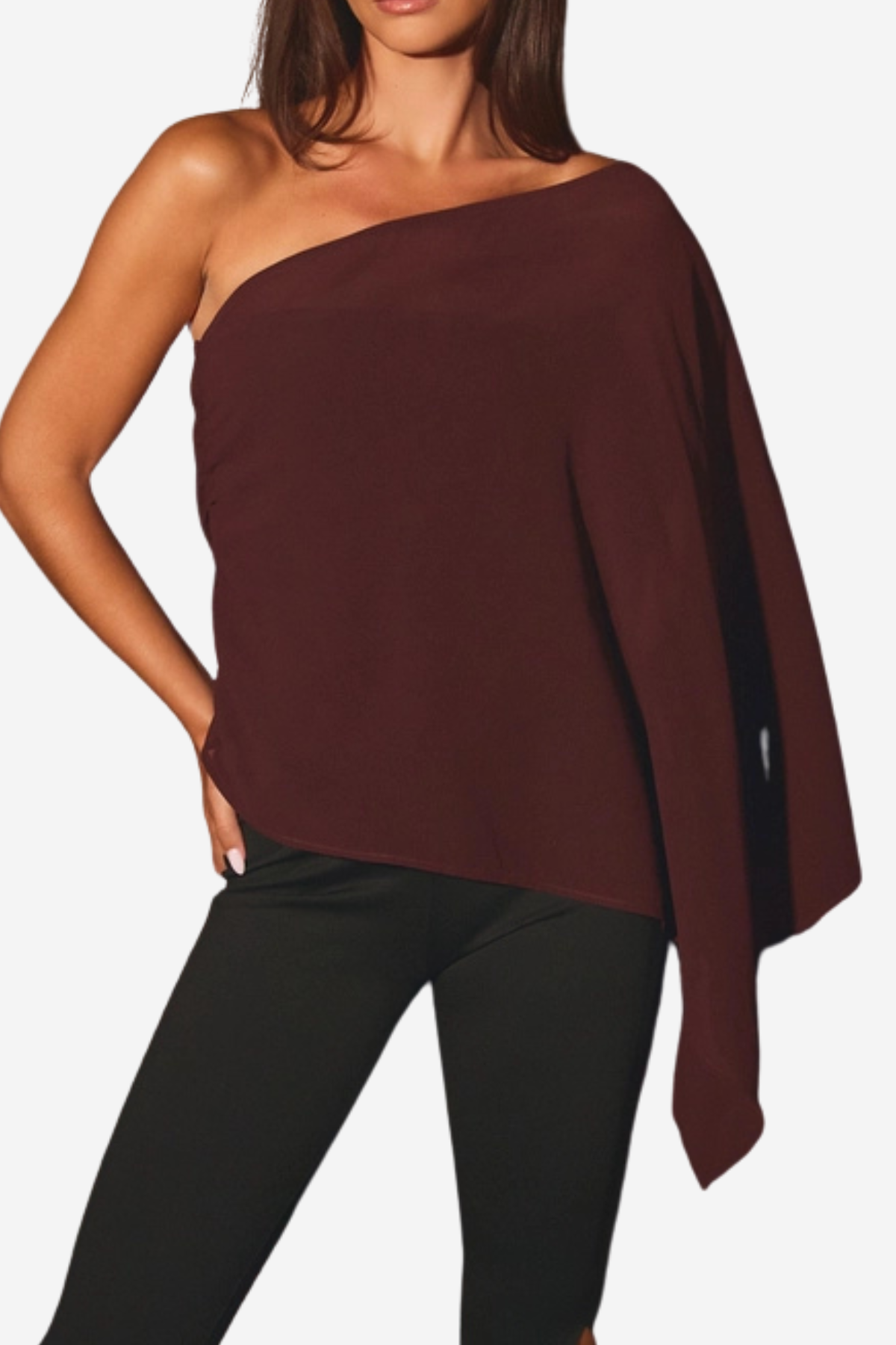 A woman wearing a dark burgundy one-shoulder knit poncho top with black leggings, shown from the neck down against a light gray background.