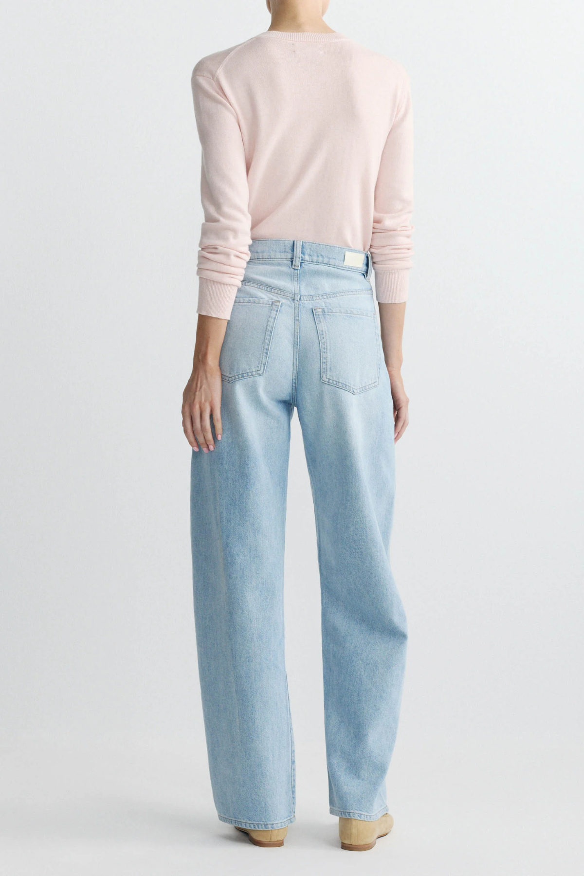 Person wearing light blue jeans and a pink sweater on a white background