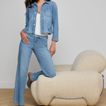 Woman in denim outfit standing next to a modern chair against a plain background