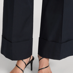 Black strappy high-heel sandals worn with dark navy wide-leg trousers, shown from the calves down on a light gray studio background.