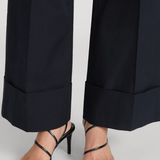 Black strappy high-heel sandals worn with dark navy wide-leg trousers, shown from the calves down on a light gray studio background.