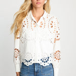 Woman wearing a white blouse with cut-out patterns and blue jeans on a light gray background