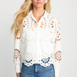 Woman wearing a white blouse with cut-out patterns and blue jeans on a light gray background