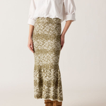 Woman wearing a white blouse and patterned skirt with brown boots on a white background