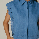 Woman wearing a blue sleeveless blouse with scalloped edges on a plain background