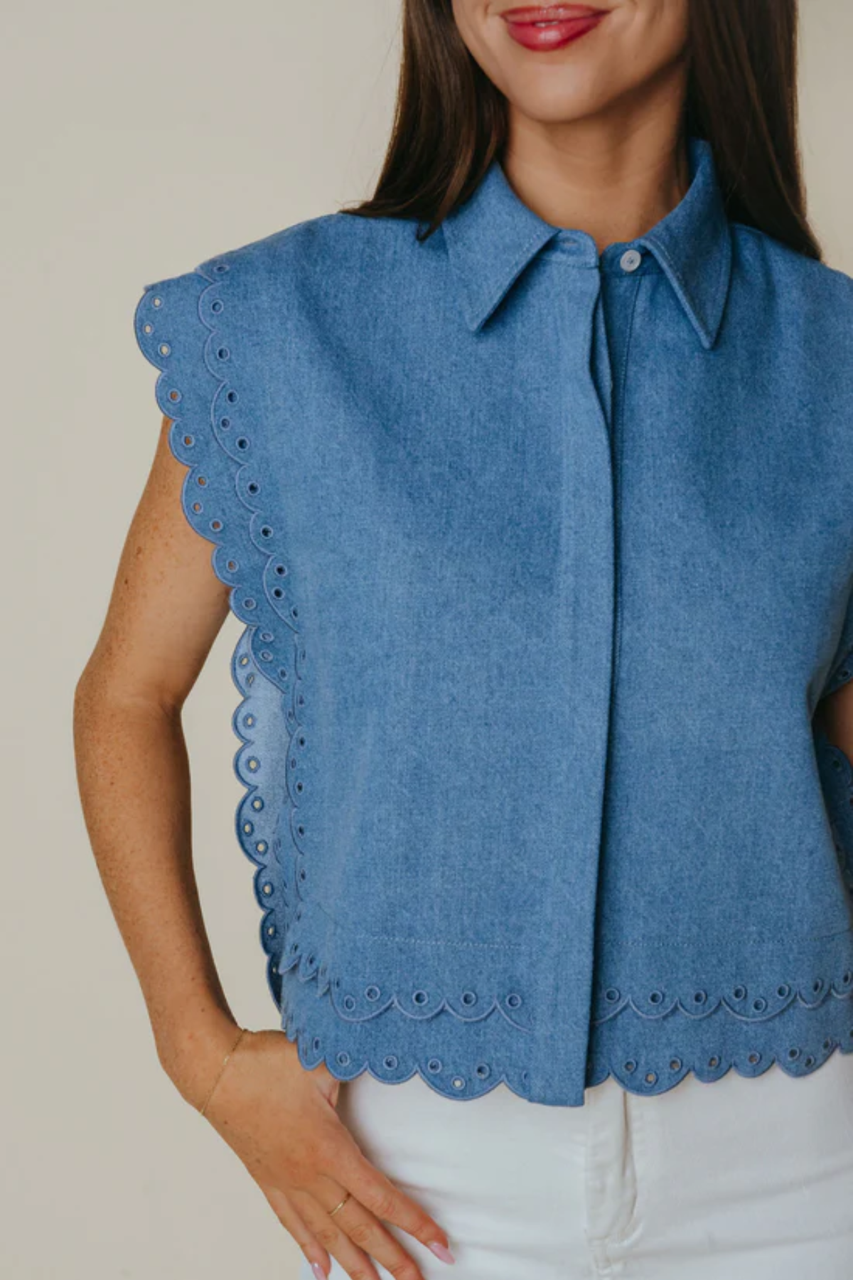 Woman wearing a blue sleeveless blouse with scalloped edges on a plain background