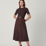 Woman wearing a brown dress with a belt and brown boots on a light gray background