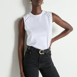 Woman wearing a white sleeveless top with decorative elements and black pants against a white background