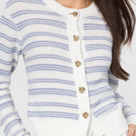 Woman wearing a white cardigan with blue stripes and gold buttons on a light gray background