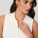 Woman wearing a white sleeveless top against a plain background