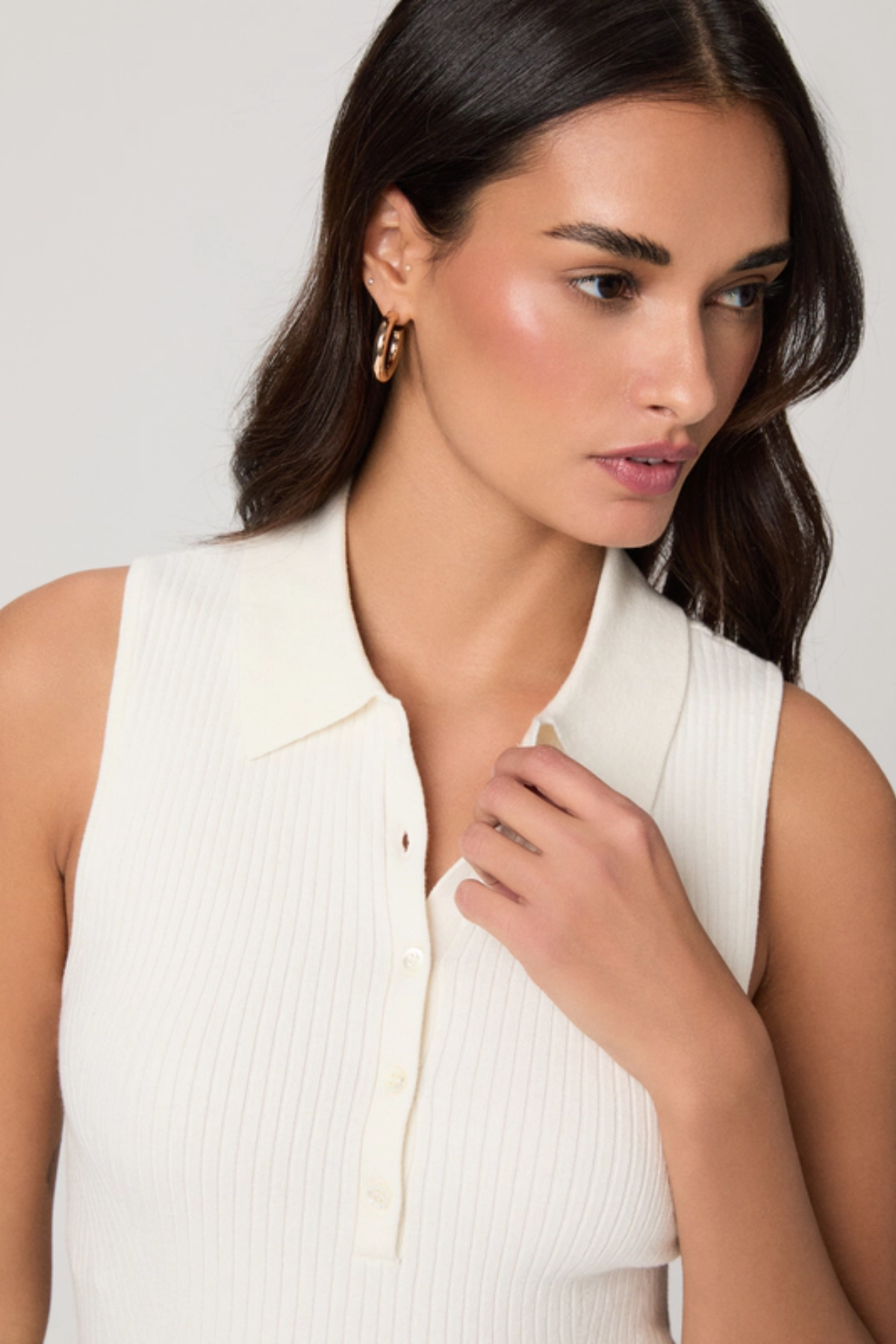 Woman wearing a white sleeveless top against a plain background