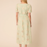 Woman wearing a light green dress with floral embroidery on a beige background