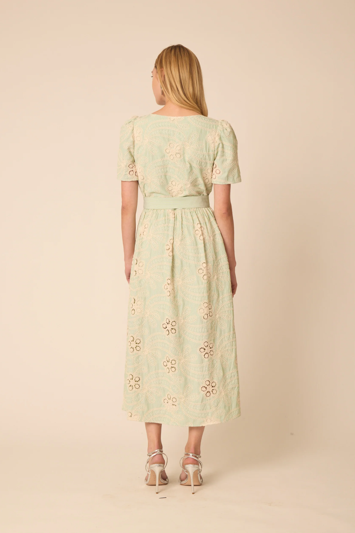Woman wearing a light green dress with floral embroidery on a beige background