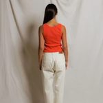Person wearing a red top and white pants standing against a plain background