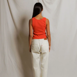 Person wearing a red top and white pants standing against a plain background