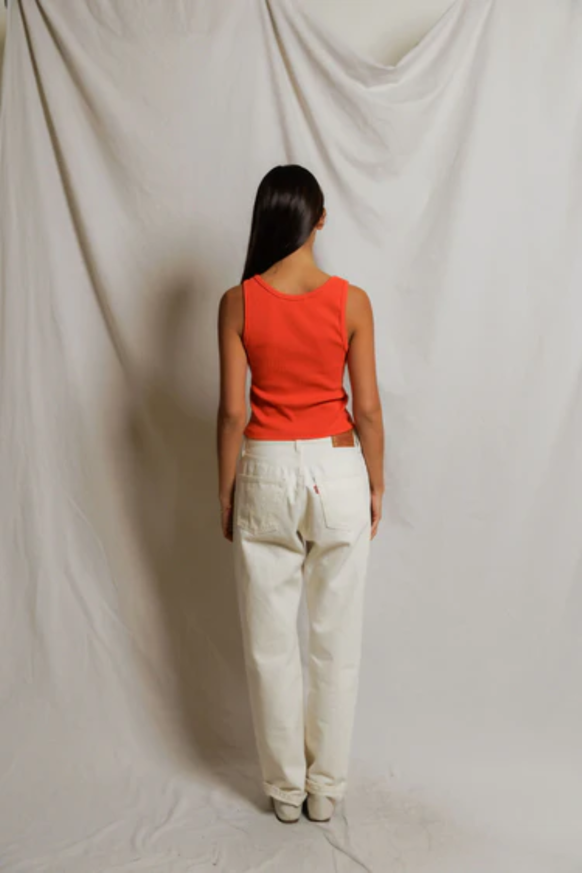 Person wearing a red top and white pants standing against a plain background