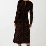 A woman shown from the back wearing a long-sleeve dark brown velvet dress with an intricate floral jacquard pattern, paired with black lace-up heels, against a plain white studio background.