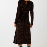 A woman shown from the back wearing a long-sleeve dark brown velvet dress with an intricate floral jacquard pattern, paired with black lace-up heels, against a plain white studio background.
