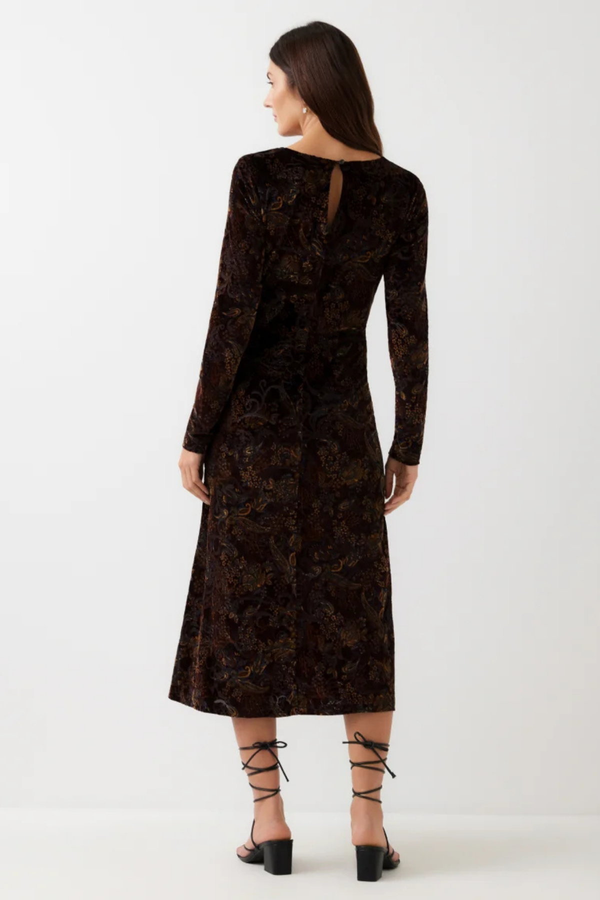 A woman shown from the back wearing a long-sleeve dark brown velvet dress with an intricate floral jacquard pattern, paired with black lace-up heels, against a plain white studio background.