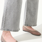 Person wearing gray jeans and pink flats on a white background